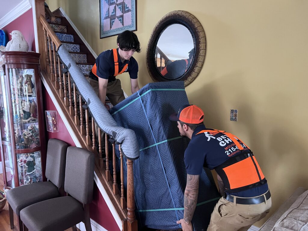 Better Choice Moving crew carrying wrapped furniture past a padded banister