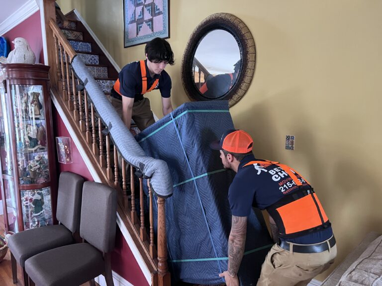 Better Choice Moving crew carrying wrapped furniture past a padded banister